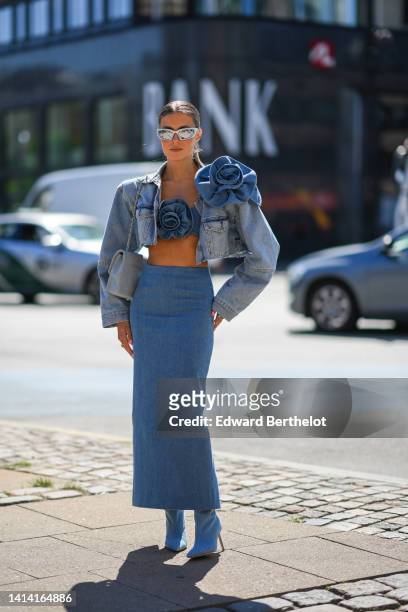 Guest wears silver sunglasses, a blue denim with large embroidered flower / shoulder-off / cropped top, a matching blue faded denim with a large...