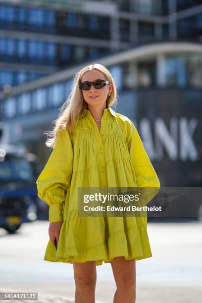 Guest wears dark brown sunglasses, gold and green earrings, a gold chain necklace, a silver and rhinestones necklace, a yellow pleated / ruffled /...