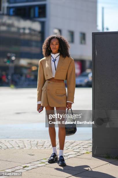 Guest wears gold earrings, a black shiny leather laces tie from Prada, a white cropped shirt from Miu Miu, a brown linen cropped blazer jacket, a...