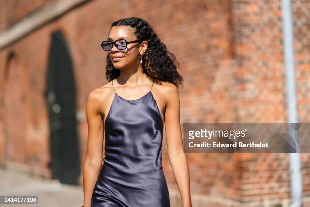 Guest wears black and blue sunglasses, gold and pearl pendant earrings, a dark gray to black gradient print pattern halter-neck silk long dress,...