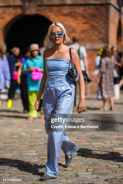 Guest wears silver sunglasses, silver large earrings, a black shiny leather with embroidered rhinestones tube shoulder bag, a pale blue shiny leather...