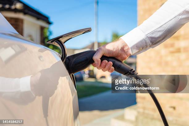 man charging electric car at home - electric car home stock pictures, royalty-free photos & images