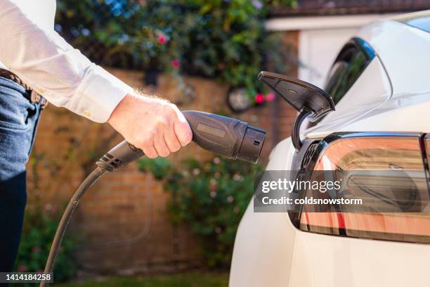 man charging electric car at home - fuel efficient stock pictures, royalty-free photos & images