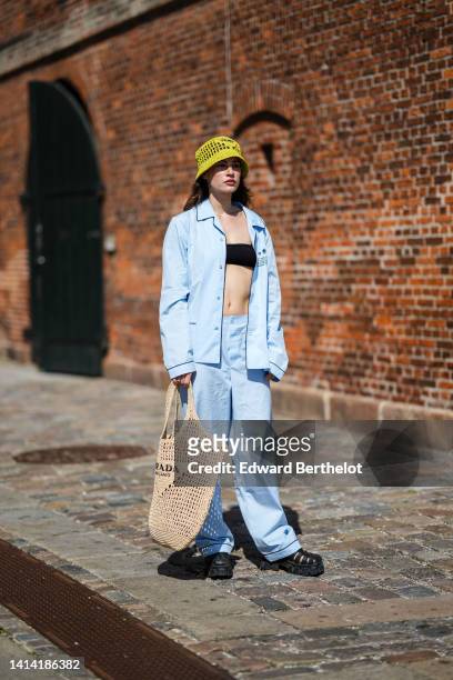Guest wears a yellow fishnet / mesh bob hat from Prada, a black shoulder-off / cropped top, a pale blue cotton shirt, matching pale blue cotton large...