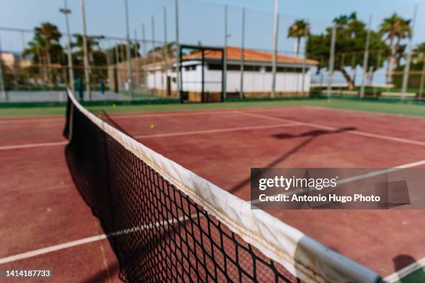 tennis net on a reddish-colored tennis court - tennis net fotografías e imágenes de stock