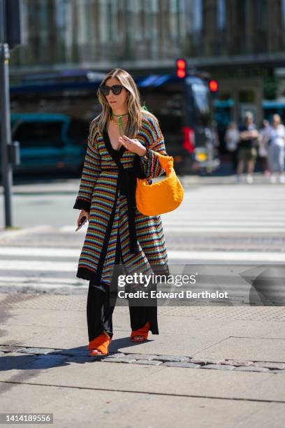 Guest wears black sunglasses, a neon green bob, a gold large chain necklace, a multicolored striped print pattern fishnet / mesh / wool long belted...