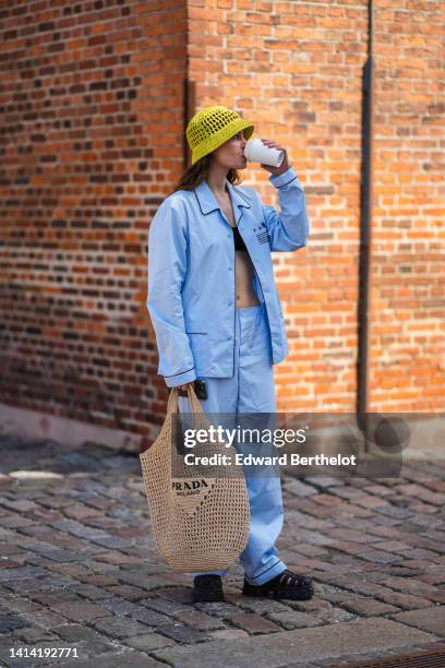 Guest wears a yellow fishnet / mesh bob hat from Prada, a black shoulder-off / cropped top, a pale blue cotton shirt from Prada, matching pale blue...