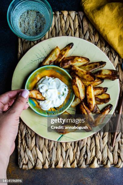 overhead view of a woman eating baked potato wedges with sour cream, garlic and dill dip - potato wedges stock pictures, royalty-free photos & images