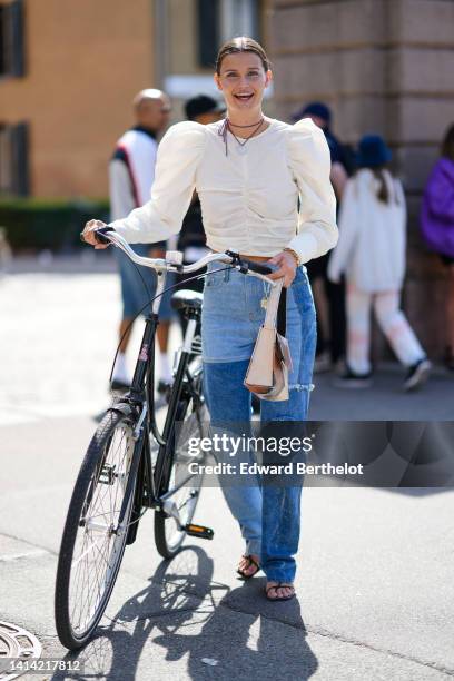 Guest wears a white cordon with large silver circle pendant necklace, a white latte ruffled / puffy shoulder / long sleeves blouse, blue bicolored...