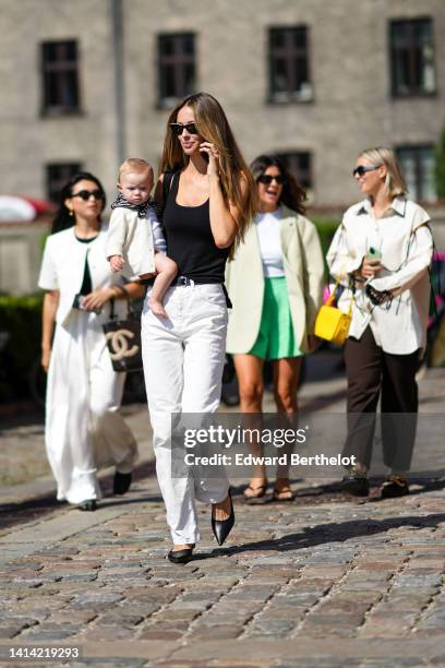 Guest wears black sunglasses, a black tank-top, white denim large pants, black shiny leather pointed pumps heels shoes , outside OperaSport, during...