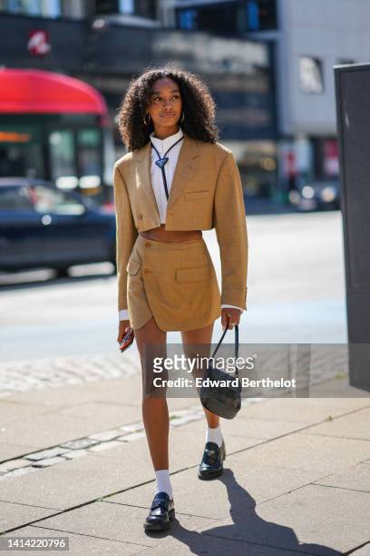 Guest wears gold earrings, a black shiny leather laces tie from Prada, a white cropped shirt from Miu Miu, a brown linen cropped blazer jacket, a...