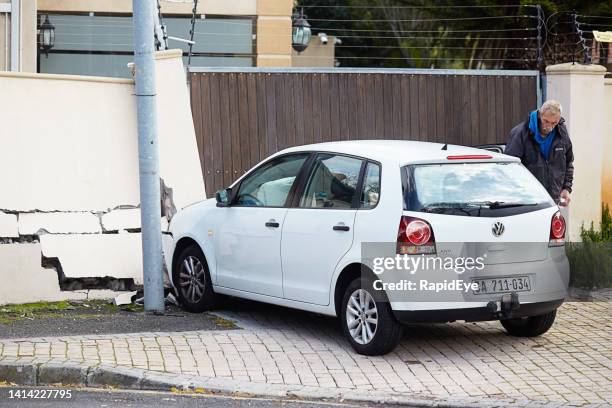 man beside car in aftermath of traffic accident that damaged the boundary wall of a house - car crash wall stock pictures, royalty-free photos & images