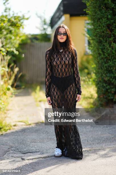 Guest wears black sunglasses, silver earrings, a silver large pendant necklace, a black lace print pattern turtleneck / long sleeves long transparent...