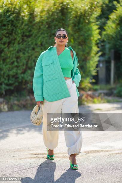 Guest wears brown sunglasses, gold earrings, a green ribbed / asymmetric cropped top, a green checkered pattern oversized jacket shirt, white latte...