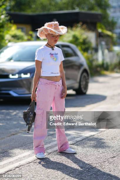 Guest wears an orange and white ripped western hat, a black pendant necklace, a white with multicolored pattern in shape of heart t-shirt, pale pink...