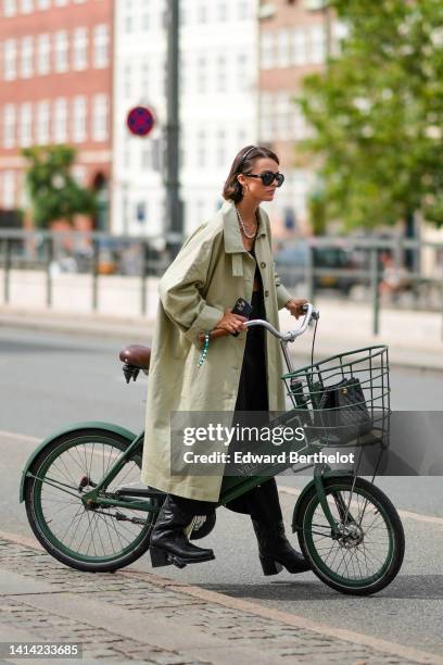 Guest wears a black headband, black sunglasses from Chanel, gold earrings, a white pearls and gold chain necklaces, a pale khaki oversized long...