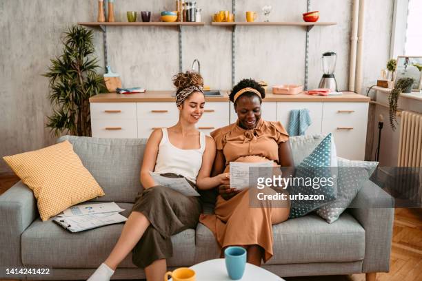 pregnant lesbian couple checking their finances on the sofa - financial planning couple stock pictures, royalty-free photos & images