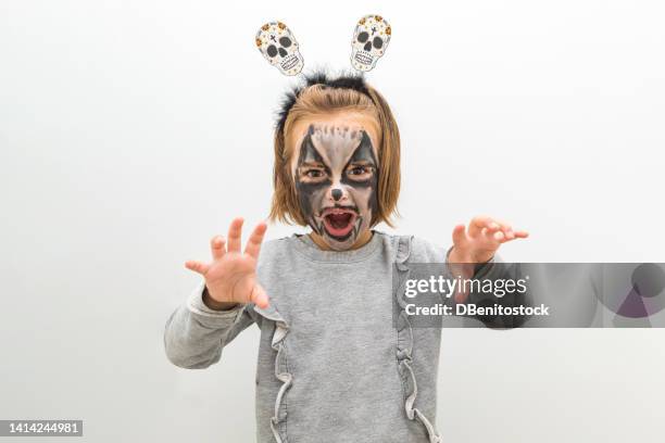 little blonde-haired girl, wearing skull and crossbones headband, vampire wolf makeup on halloween day, scaring. concept of carnival, dress up, make up and celebration of party and tradition. - children role playing crime stock-fotos und bilder