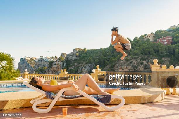 teenage boy about to jump into pool and splash his sunbathing girlfriend - holding nose stock pictures, royalty-free photos & images