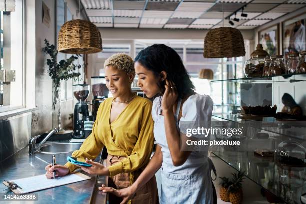 small business owners working together and writing down orders in a coffee shop. female entrepreneurs in partnership collaborating, brainstorming and planning sales for their cafe - restaurant owner stockfoto's en -beelden