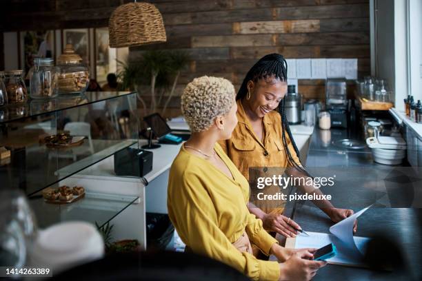 small business owner training new employee on the job at a coffee shop. black female entrepreneurs in a partnership collaborating and planning finance and growth together inside the cafe - busy coffee shop stockfoto's en -beelden