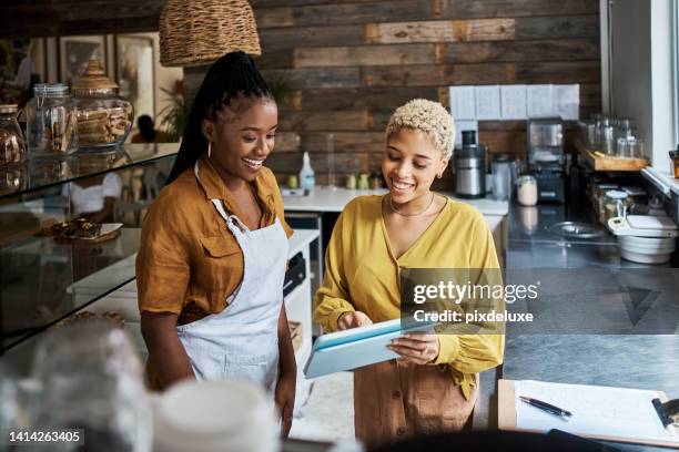 coffee shop manager, owner and supervisor using a tablet to train a waitress in her shop. workers talking while checking online orders and using a mobile app for social media ads in a cafe - restaurant staff stock pictures, royalty-free photos & images