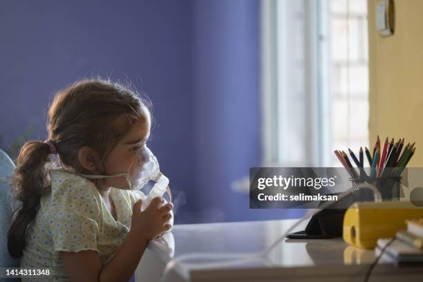 petite fille utilisant un nébuliseur tout en regardant des vidéos sur un téléphone intelligent - équipement d'assistance respiratoire photos et images de collection