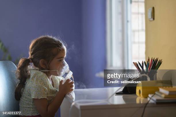 niña pequeña usando nebulizador mientras ve videos en un teléfono inteligente - nebulizador fotografías e imágenes de stock