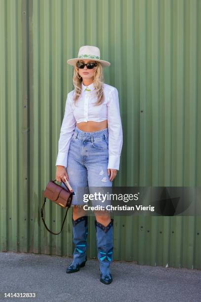 Guest is seen wearing hat, cut off denim jeans, cowboy boots, brown Jacquemus bag outside Stine Goya during Copenhagen Fashion Week Spring/Summer...