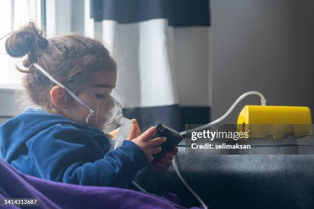 toddler girl using nebulizer while watching videos on smart phone - breathing device stock pictures, royalty-free photos & images