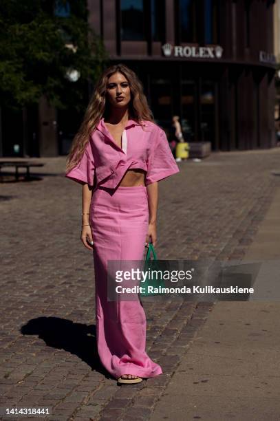 Emili Sindlev wearing long pink maxi skirt and matching shirt sleeve crop top and carrying green bag posing outside Holzweiler during Copenhagen...