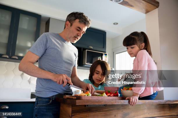 loving daddy chopping vegetables to snack with his son and daughter at home - chopping stock pictures, royalty-free photos & images