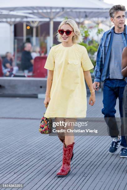 Emma Chamberlain seen wearing yellow dress, red cowboy boots, bag with floral print outside Ganni during Copenhagen Fashion Week Spring/Summer 2023...