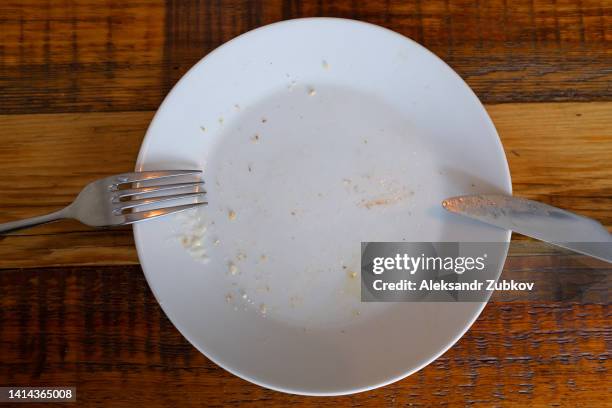 a dirty empty plate, fork and knife on a wooden table. cutlery is used, symbolizing the end of lunch or dinner. food and drink establishment, cafe or restaurant, home cooking. - kitchen after party foto e immagini stock