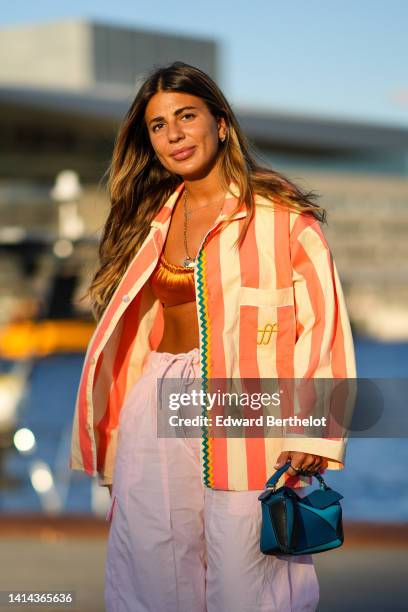 Héloïse Salessy wears gold and white small pearls earrings, a gold pendants necklace, a shiny orange square-neck / cropped swimwear as a tank-top, a...