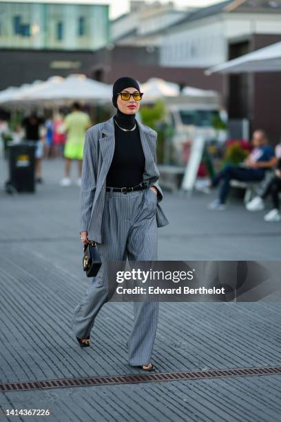 Guest wears a black scarf as a headband, black and yellow sunglasses, a black turtleneck pullover, a gold necklace, a gray and small white striped...