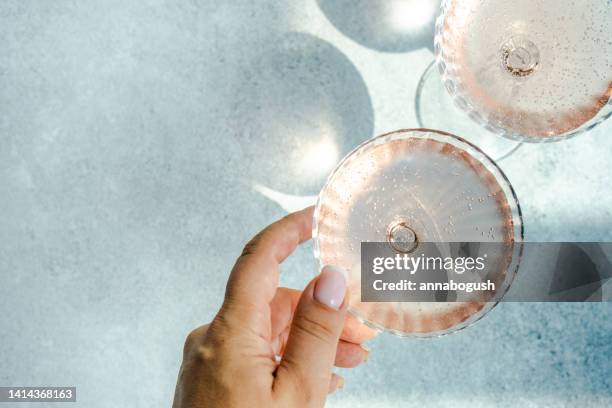 woman reaching for two glasses of pink champagne in champagne coupe glasses - prosecco glas stock-fotos und bilder