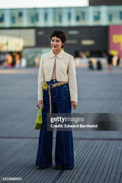 Alyssa Coscarelli wears a beige matte cropped blazer jacket, high waist navy blue denim wide legs pants, a purple and yellow braided fabric belt, a...