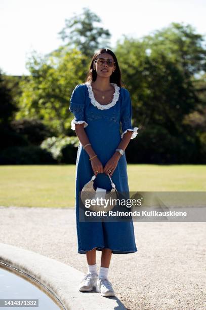 Babba C Rivera wearing blue denim dress with white collar, brown sunglasses, white sneakers and light brown bag posing outside Skall Studio during...