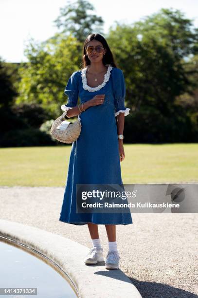 Babba C Rivera wearing blue denim dress with white collar, brown sunglasses, white sneakers and light brown bag posing outside Skall Studio during...