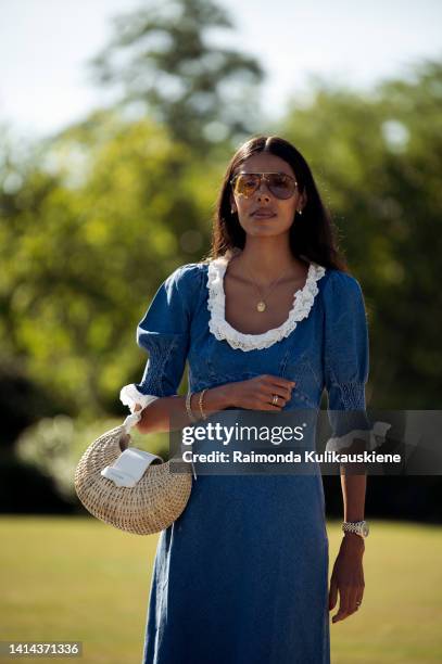 Babba C Rivera wearing blue denim dress with white collar, brown sunglasses, white sneakers and light brown bag posing outside Skall Studio during...