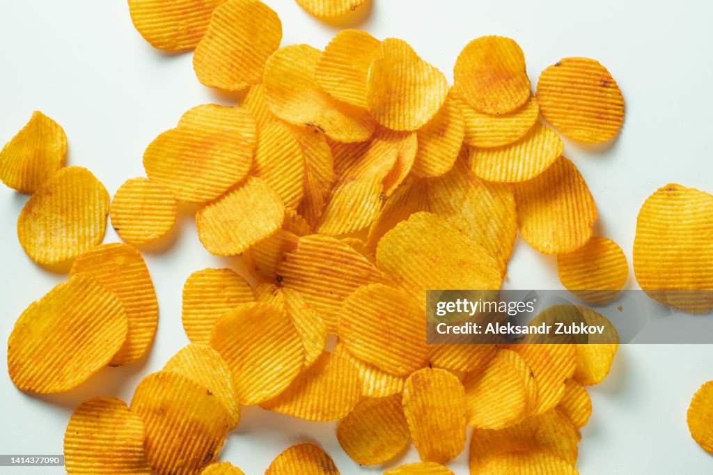 Crispy fried potato chips are scattered on a white background or table. Corn spicy fatty chips with paprika and spices. The concept of unhealthy diet and lifestyle, accumulation of excess weight. Copy space. Background of food.