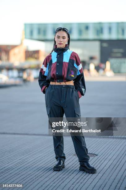 Guest wears black glasses, silver earrings, a black / blue / burgundy cropped rain jacket from Ganni, black cargo pants from Ganni, black shiny...