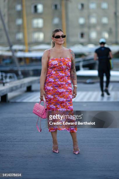 Guest wears black sunglasses, silver earrings, an orange with blue / pink / white flower print pattern ruffled / square-neck / tank-top / tube midi...