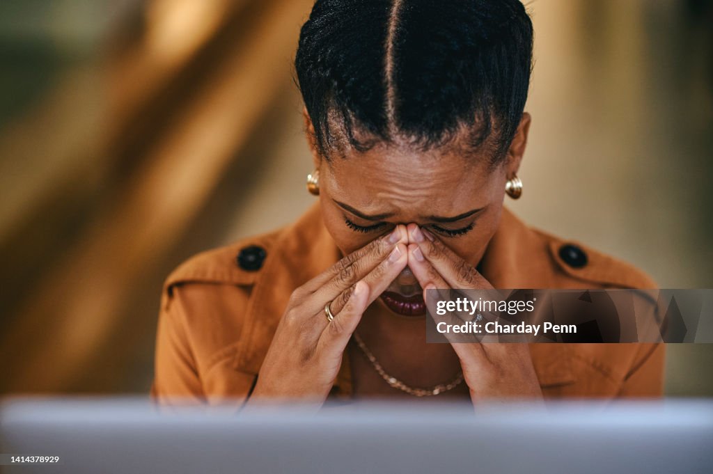 Tired and stressed businesswoman with a headache from burnout of working and looking at her laptop screen. Frustrated female manager sad and crying at her desk in her modern office in the evening