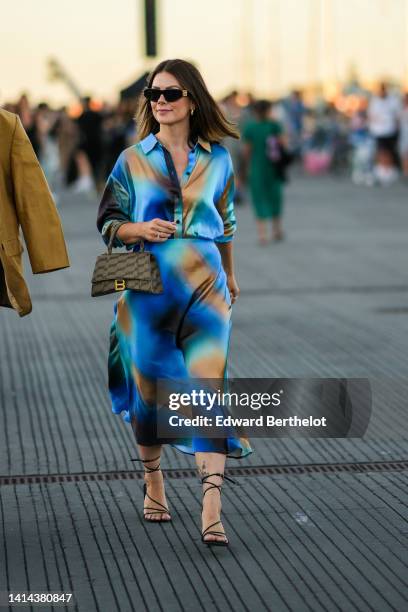 Guest wears black sunglasses from Balenciaga, a camel / blue / black tie and dye print pattern silk shirt / long sleeves / long dress, a brown and...