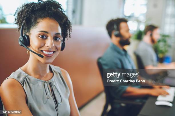 african american female sales team leader or customer service agent working in a call center, talking to a client with a headset. happy business woman office with diverse colleagues in background. - phone operators stock pictures, royalty-free photos & images