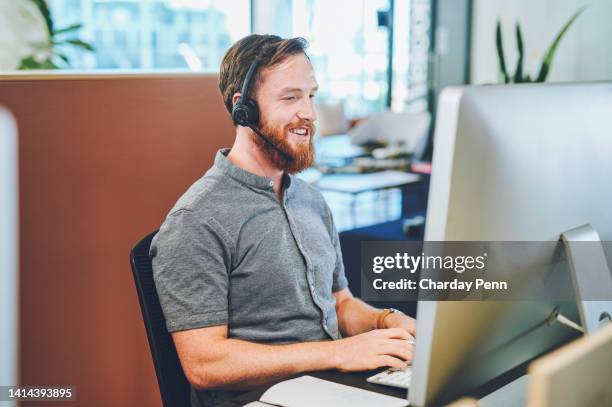 male call center agent on a computer working, happy and smiling while talking to a client on a headset in a modern office. young professional online hotline service operator giving a customer advice - headset imagens e fotografias de stock