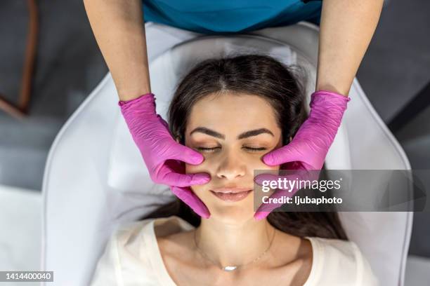 il chirurgo estetico esamina il viso della bella donna, lo tocca con le mani guantate. - chirurgia estetica donna foto e immagini stock