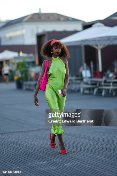Guest wears a red large headband, gold earrings, a green halter-neck / sleeveless / long silk dress, a neon pink sponge shoulder bag, red quilted...